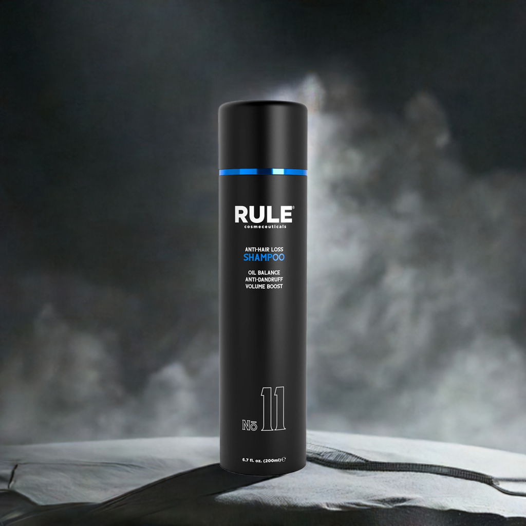 Rule No. 11 Anti-Hair Loss Shampoo bottle, emphasizing oil balance, anti-dandruff, and volume boost benefits, set against a textured surface with a dramatic, smoky background for a sleek and modern look.