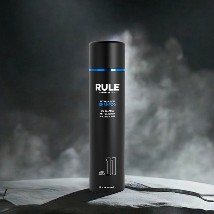 Rule No. 11 Anti-Hair Loss Shampoo bottle, emphasizing oil balance, anti-dandruff, and volume boost benefits, set against a textured surface with a dramatic, smoky background for a sleek and modern look.
